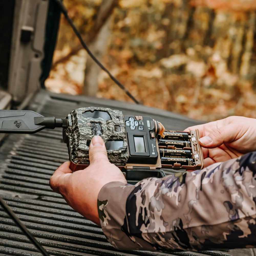 Person handling a camouflage Browning trail camera on a vehicle